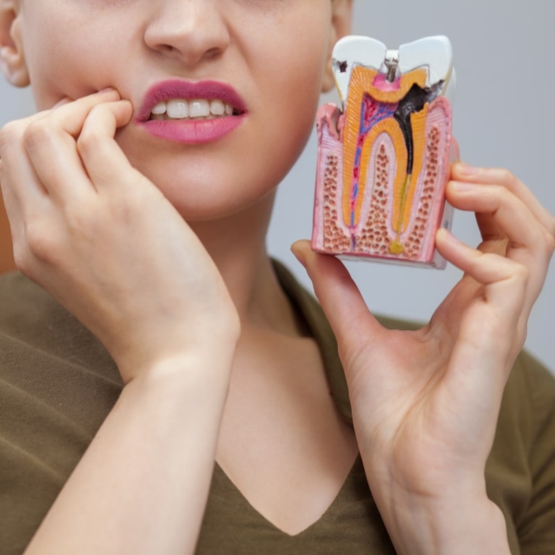 Woman with tooth pain holding tooth decay model illustrating dental emergency.