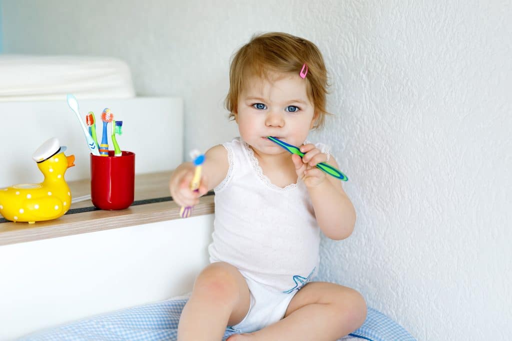 Little baby girl holding toothbrush and brushing first teeth.|when do babies get their first tooth