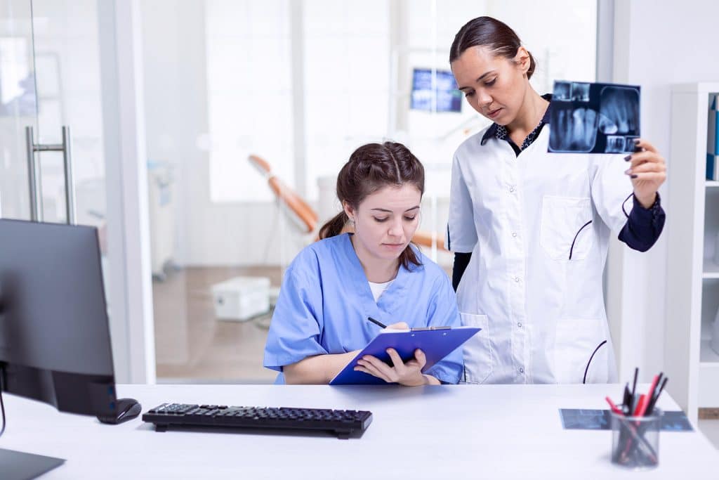 Dentist nurse taking notes about teeth hygine while doctor is holding x-ray.