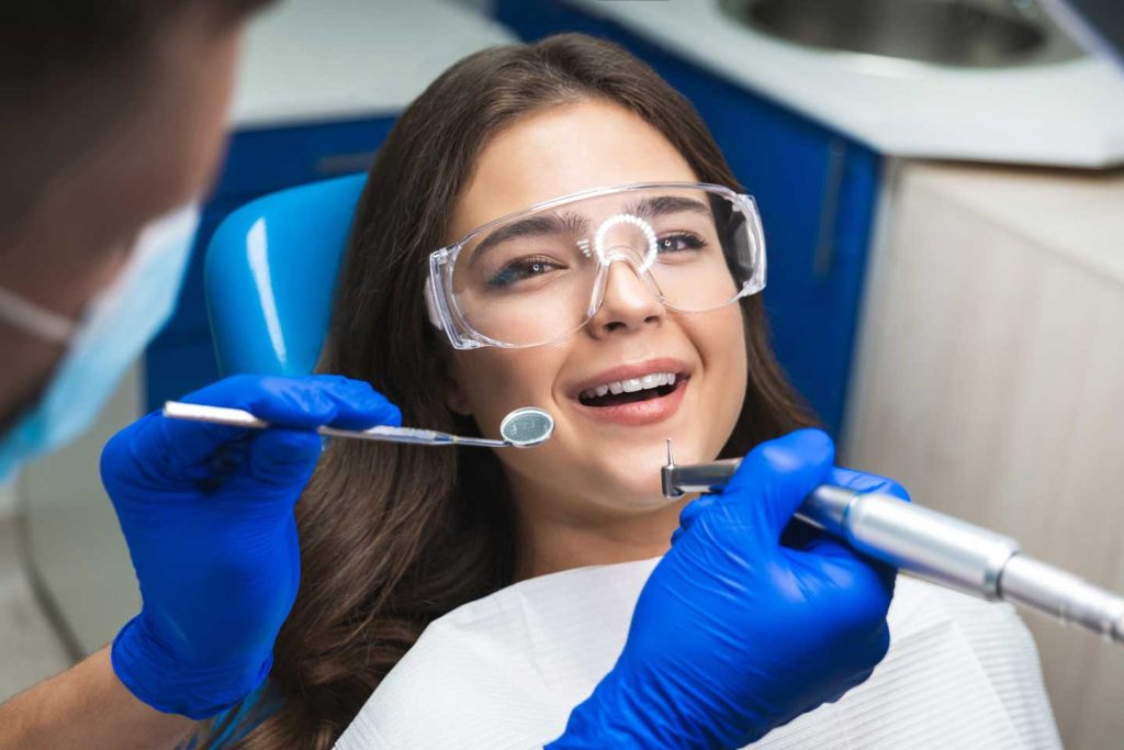 smiling patient woman in safety glasses curing bad tooth during appointment at dental clinic.