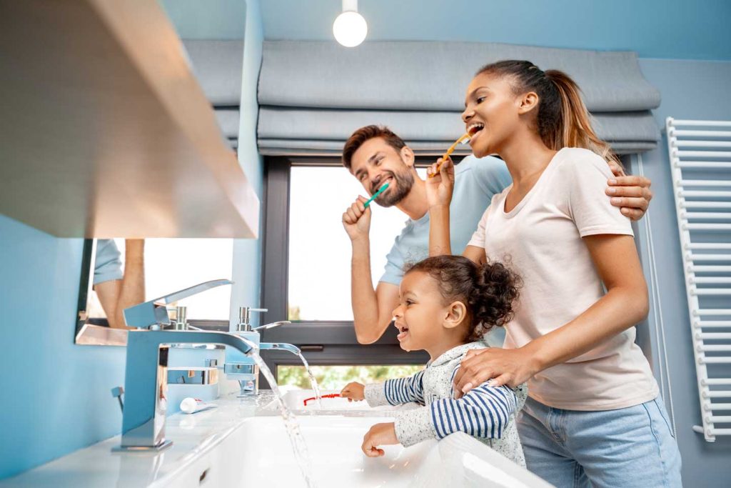 Low angle view of cheerful young adult man hugging happy woman and brushing teeth in the morning.