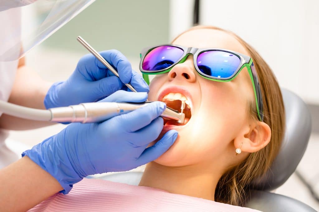 Save Download Preview Dental hygienist performing teeth cleaning procedure to a girl in pediatric dental clinic