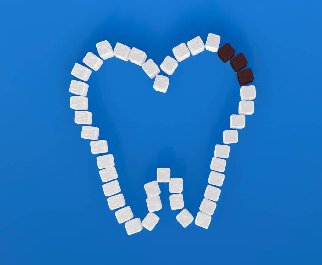Tooth symbol created from white and brown sugar cubes showcasing decay tooth on blue background|Tooth symbol created from white and brown sugar cubes showcasing decay tooth on blue background|Tooth symbol created from white and brown sugar cubes showcasing decay tooth on blue background