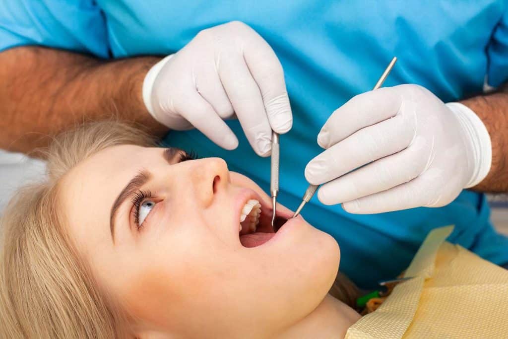 Dentist treating women's tooth extraction with help of dental tools|Dentist treating women's tooth extraction with help of dental tools