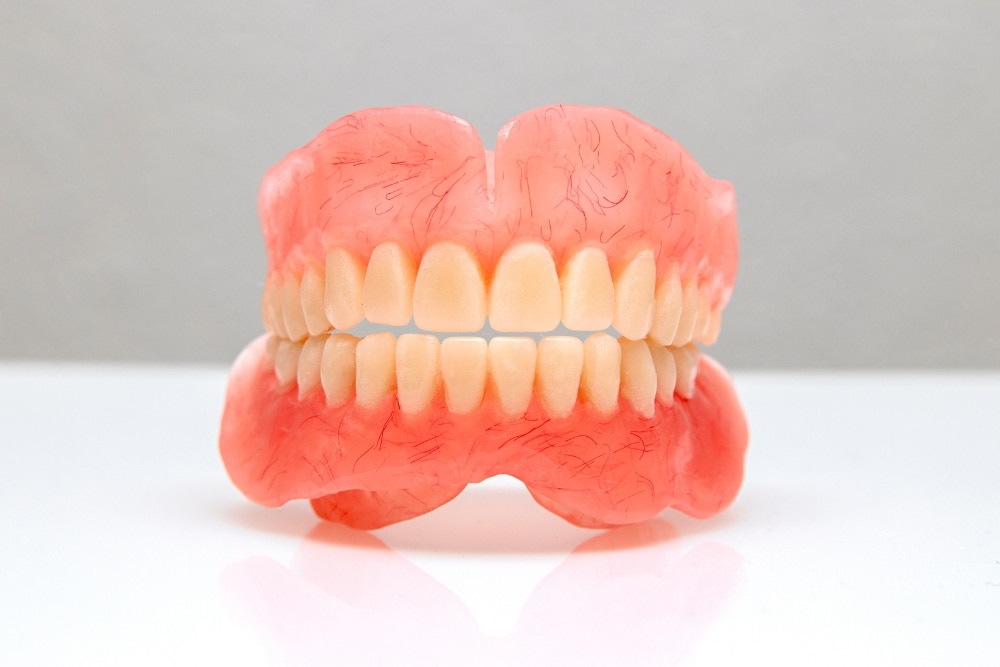 Close-up photo of a full upper digital denture in white acrylic material. The denture has realistic-looking gum tissue and teeth.