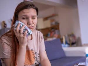 Woman holding an ice pack to reduce swelling after dental extraction.