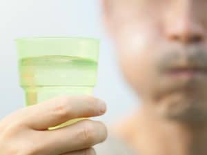 Man holds mouthwash, dealing with swelling after dental extraction.